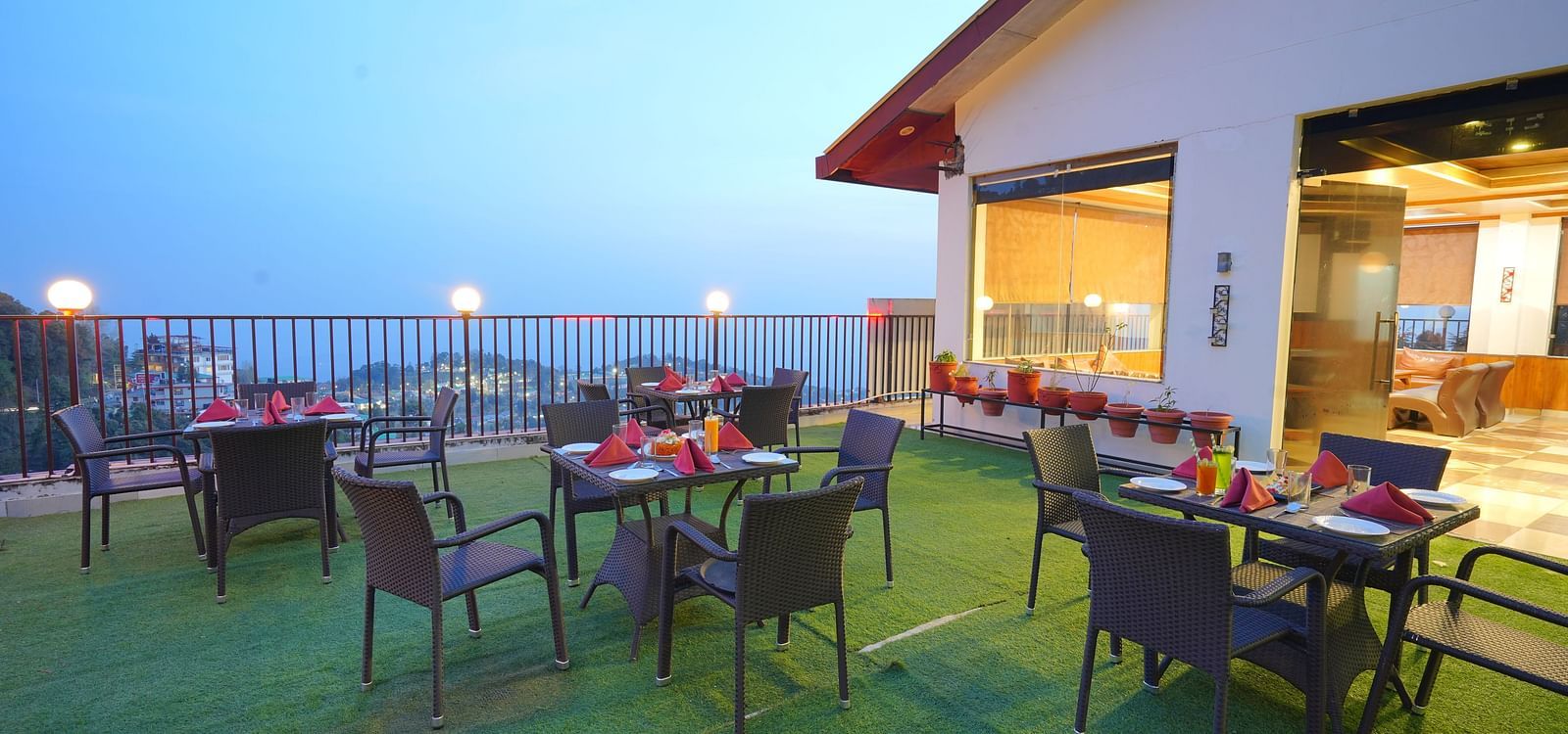 A rooftop restaurant with a scenic view. The restaurant has tables and chairs set up on a grassy area | DLS Hotel Shiva Sanctuary & Spa, Dharamshala