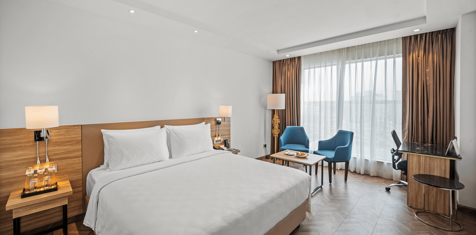 An image of a king size bed and chairs next to a huge window at Grand Vijayawada by GRT Hotels.