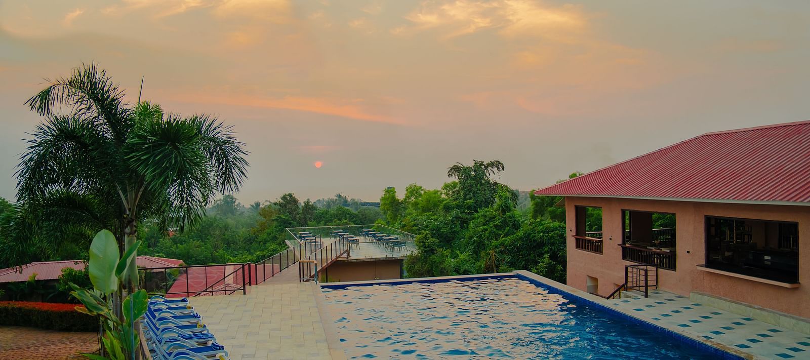 The view of a pool with beach beach chairs next to it, with the setting facing a rooftop dining section on another building - Crescent Resorts