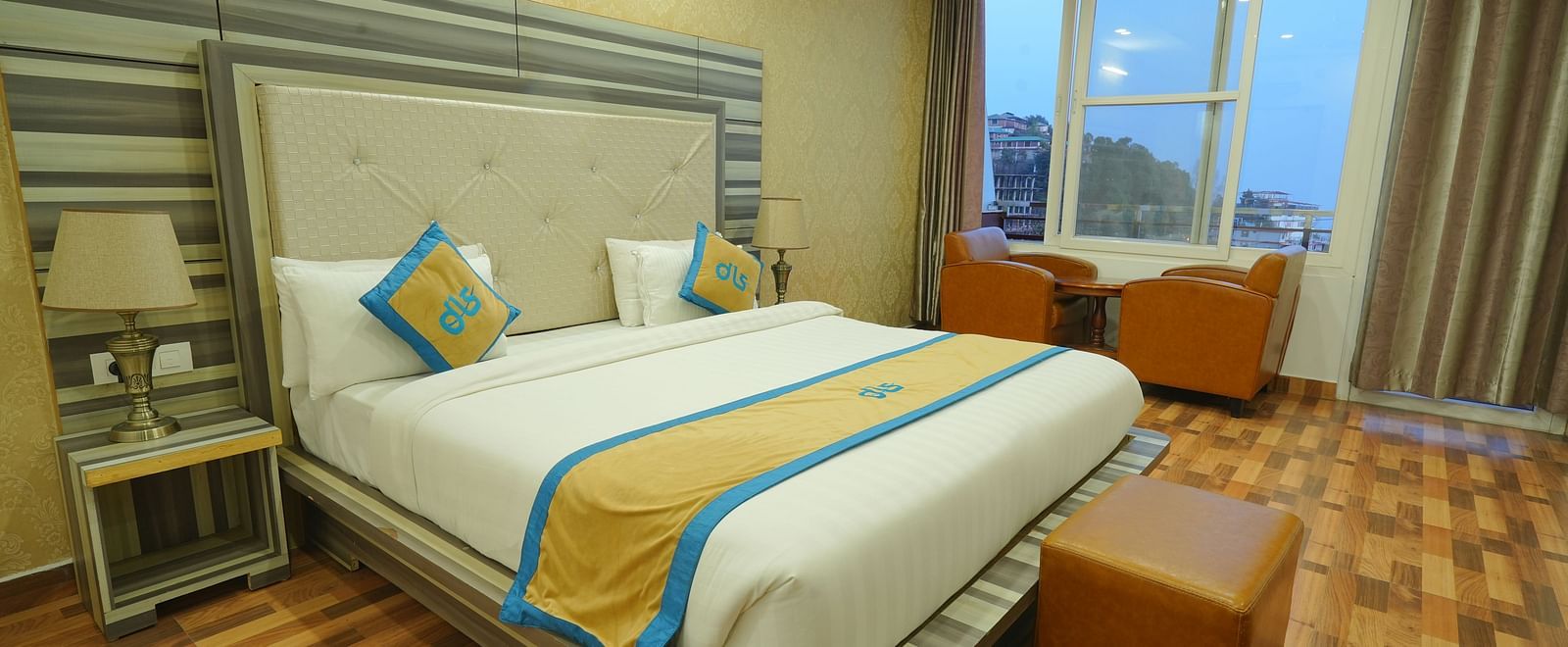 A cosy hotel room with a comfortable bed, a seating area with chairs, and a large window offering a view of the outdoors | DLS Hotel Shiva Sanctuary & Spa, Dharamshala