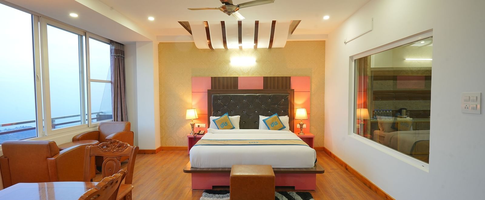 A spacious hotel room with a large bed, a seating area with a table and chairs, and large windows offering a view of the outdoors | DLS Hotel Shiva Sanctuary & Spa, Dharamshala