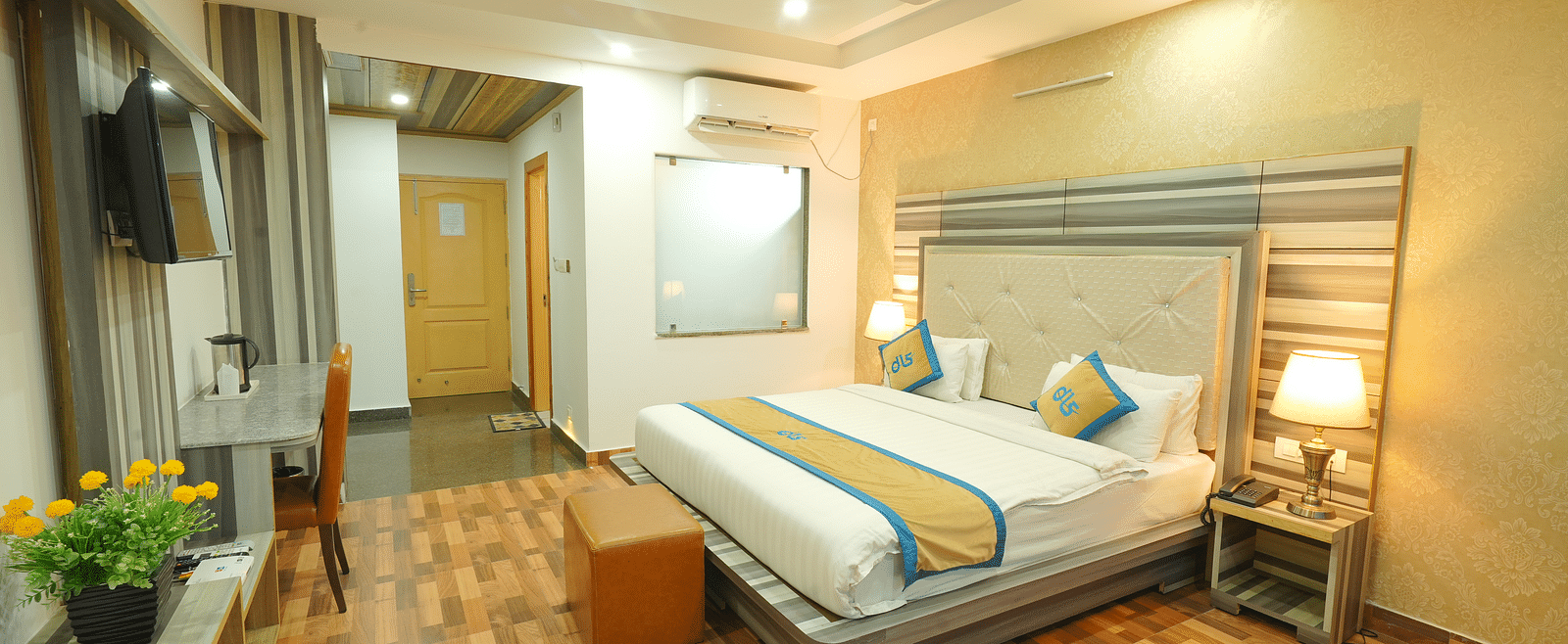 A wide angle shot of a spacious room featuring king size bed, television, wooden flooring, bed side lamp | DLS Hotel Shiva Sanctuary & Spa, Dharamshala