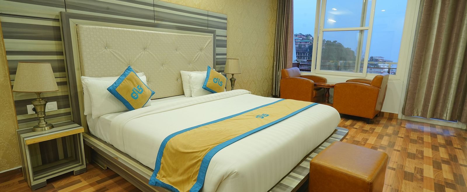 A cosy hotel room with a comfortable bed, a seating area with chairs, and a large window offering a view of the outdoors | DLS Hotel Shiva Sanctuary & Spa, Dharamshala