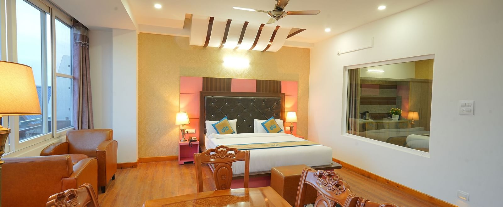 A side angle shot of the hotel suite with a king-sized bed, a seating area with a sofa, a dining table, and a flat-screen TV | DLS Hotel Shiva Sanctuary & Spa, Dharamshala