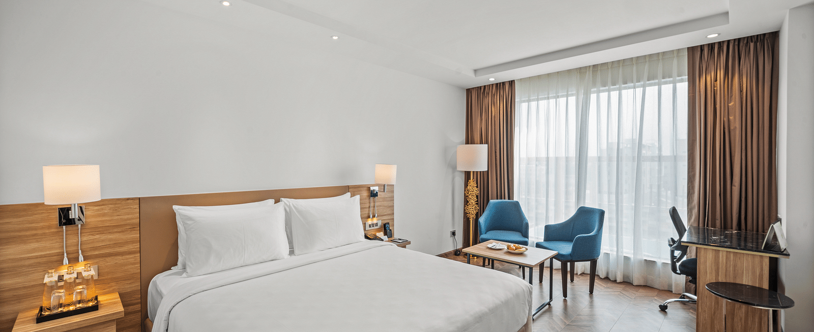 An image of a king size bed and chairs next to a huge window at Grand Vijayawada by GRT Hotels.