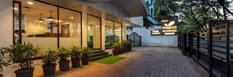 Driveway or pavement at Magnus Riverside, Kalyani Nagar featuring flower pots on one side. The ground floor of the building is made of glass walls through which we can see the interiors.