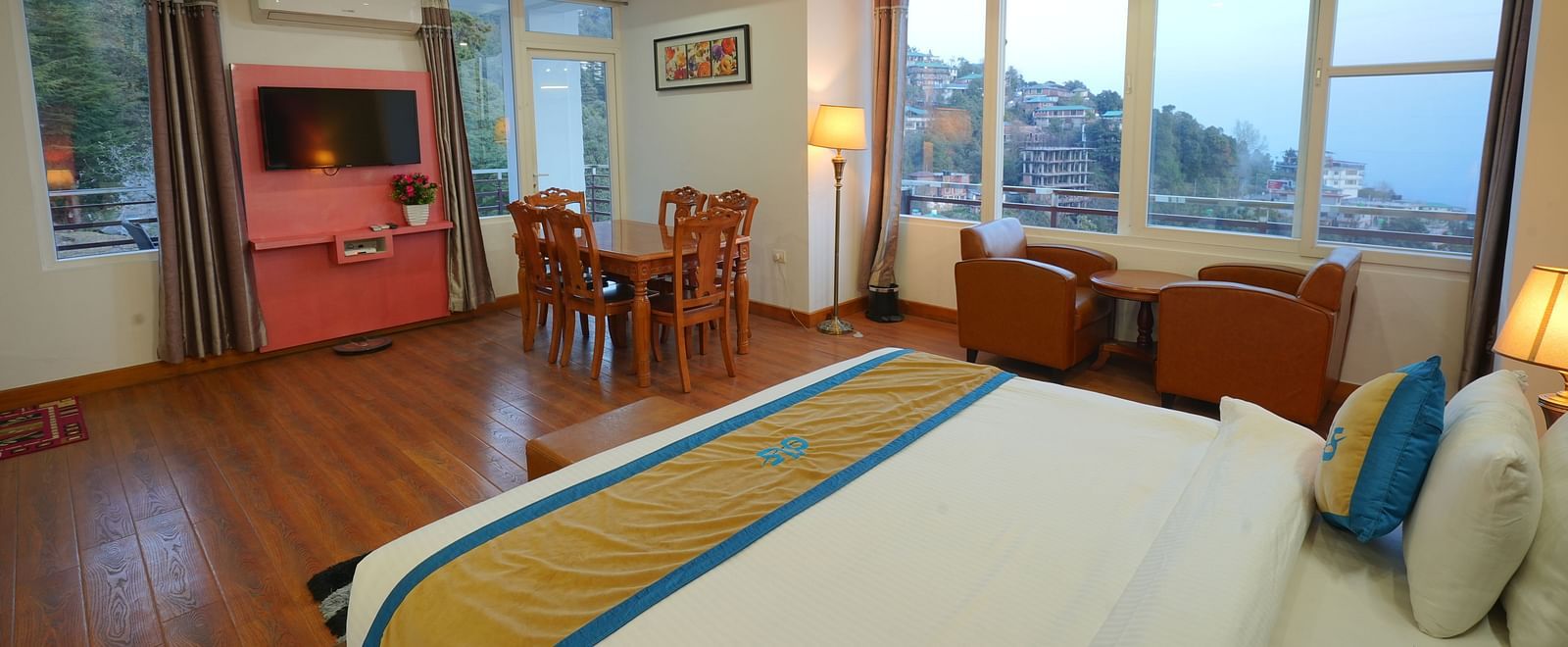 A spacious hotel suite with a king size bed, a seating area with a sofa and armchair, a dining table, and a flat-screen TV | DLS Hotel Shiva Sanctuary & Spa, Dharamshala
