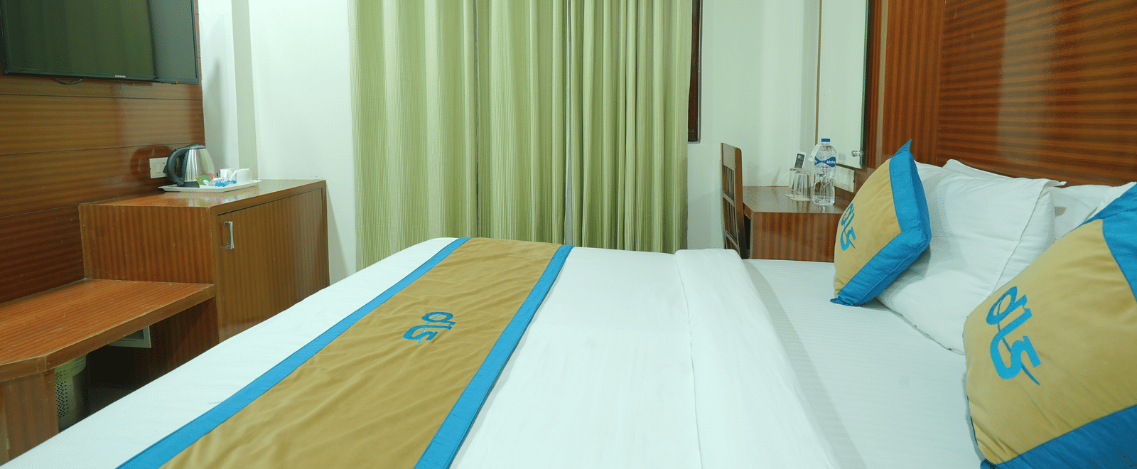 Side view of a deluxe room featuring a king size bed, a television, and a window covered by curtains at DLS Hotels The Rock Castle.