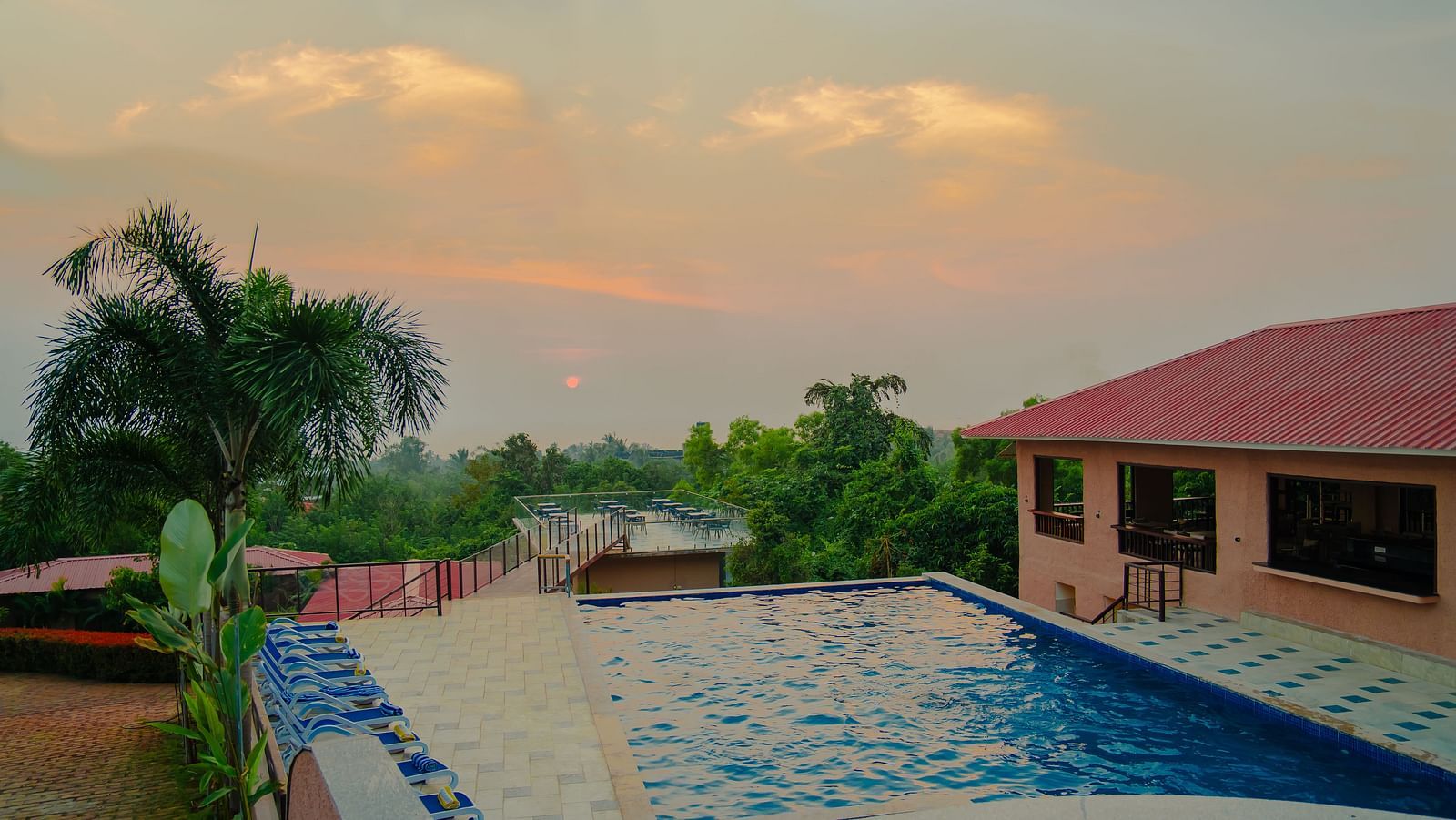 The view of a pool with beach beach chairs next to it, with the setting facing a rooftop dining section on another building - Crescent Resorts
