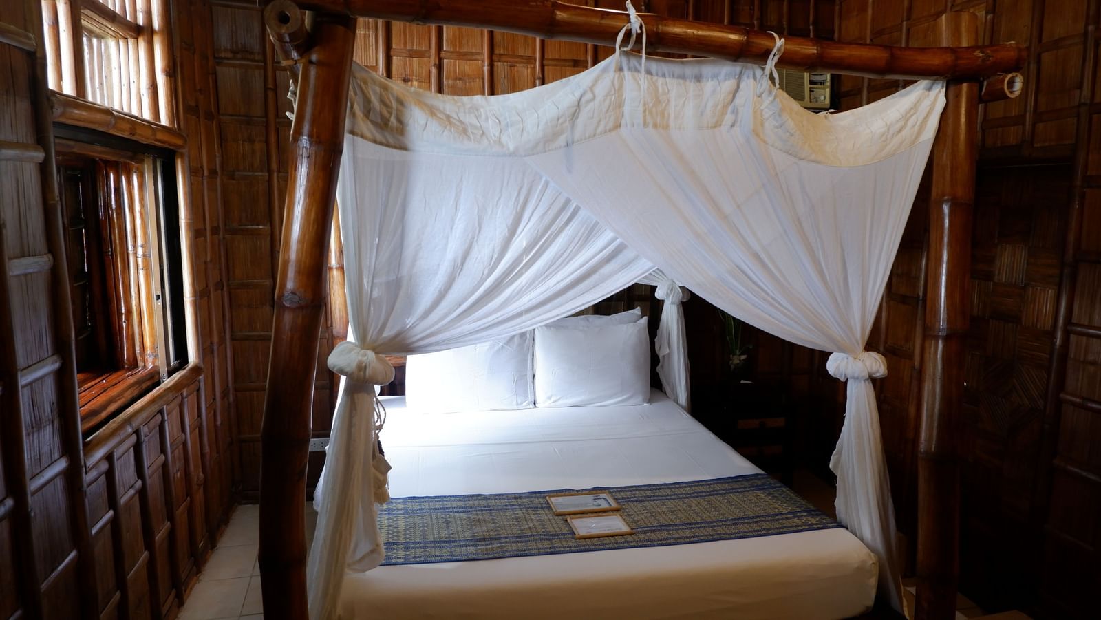 Simple bamboo room with canopy bed and large windows at Flower Island Resort.