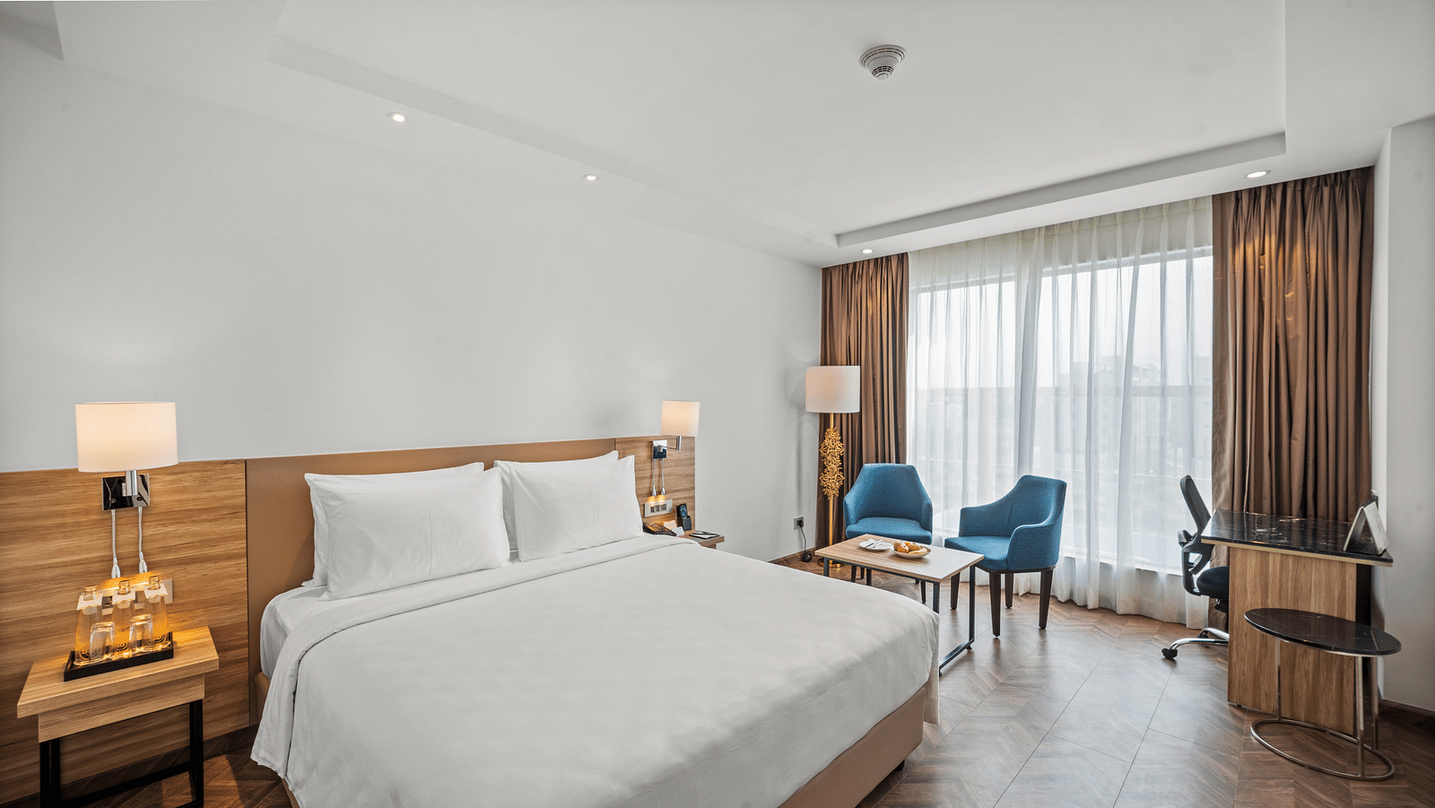 An image of a king size bed and chairs next to a huge window at Grand Vijayawada by GRT Hotels.