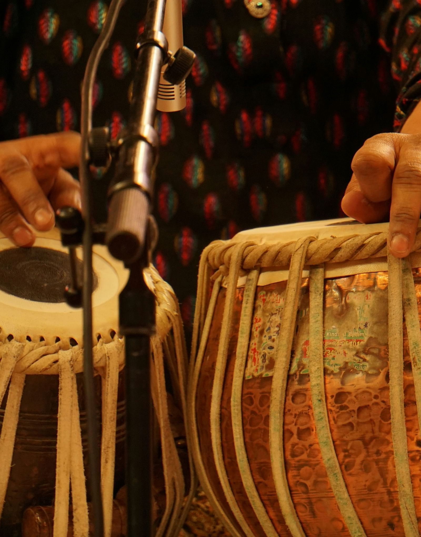 Close up shot of a person playing tabla with a mic placed in front of it.