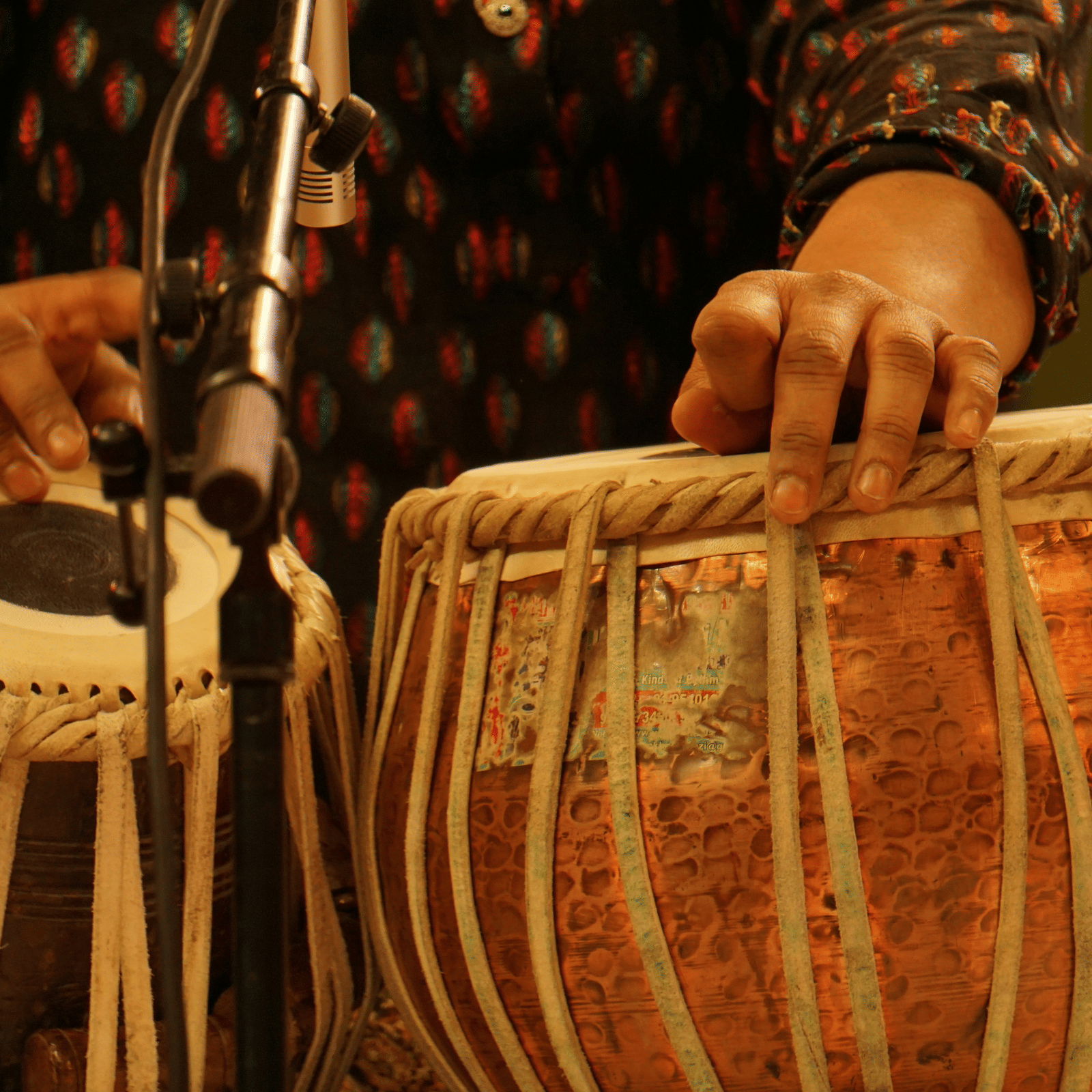 Close up shot of a person playing tabla with a mic placed in front of it.