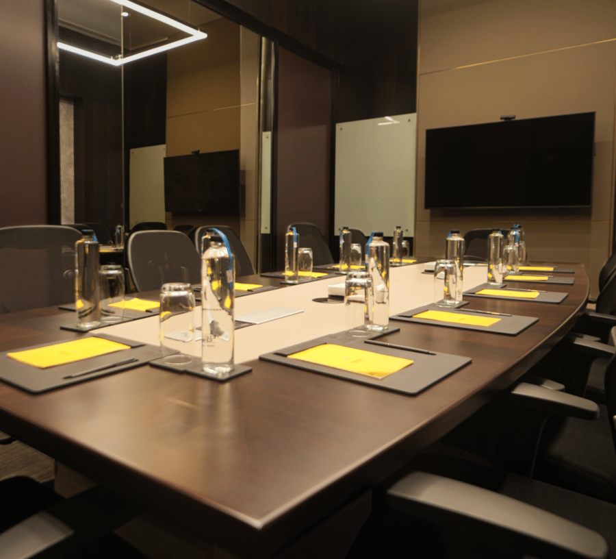 A rectangular table set with placemats cutlery and chairs arranged inside a meeting hall at The Suryaa, New Delhi.