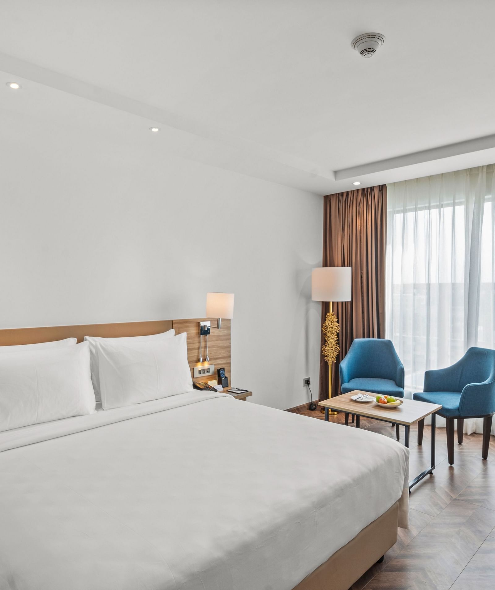 An image of a king size bed and chairs next to a huge window at Grand Vijayawada by GRT Hotels.
