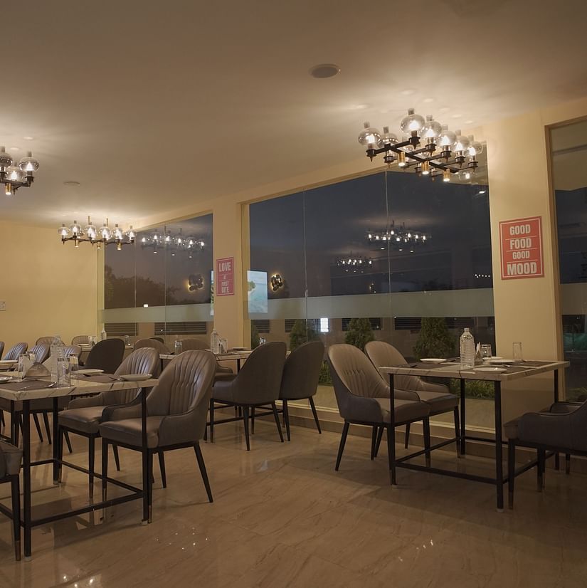 A stylish restaurant with marble tables, grey chairs, chandeliers, and large windows. Warm lighting creates a cozy, elegant ambience at Citrus Classic Resorts and Spa Mahabalipuram ECR
