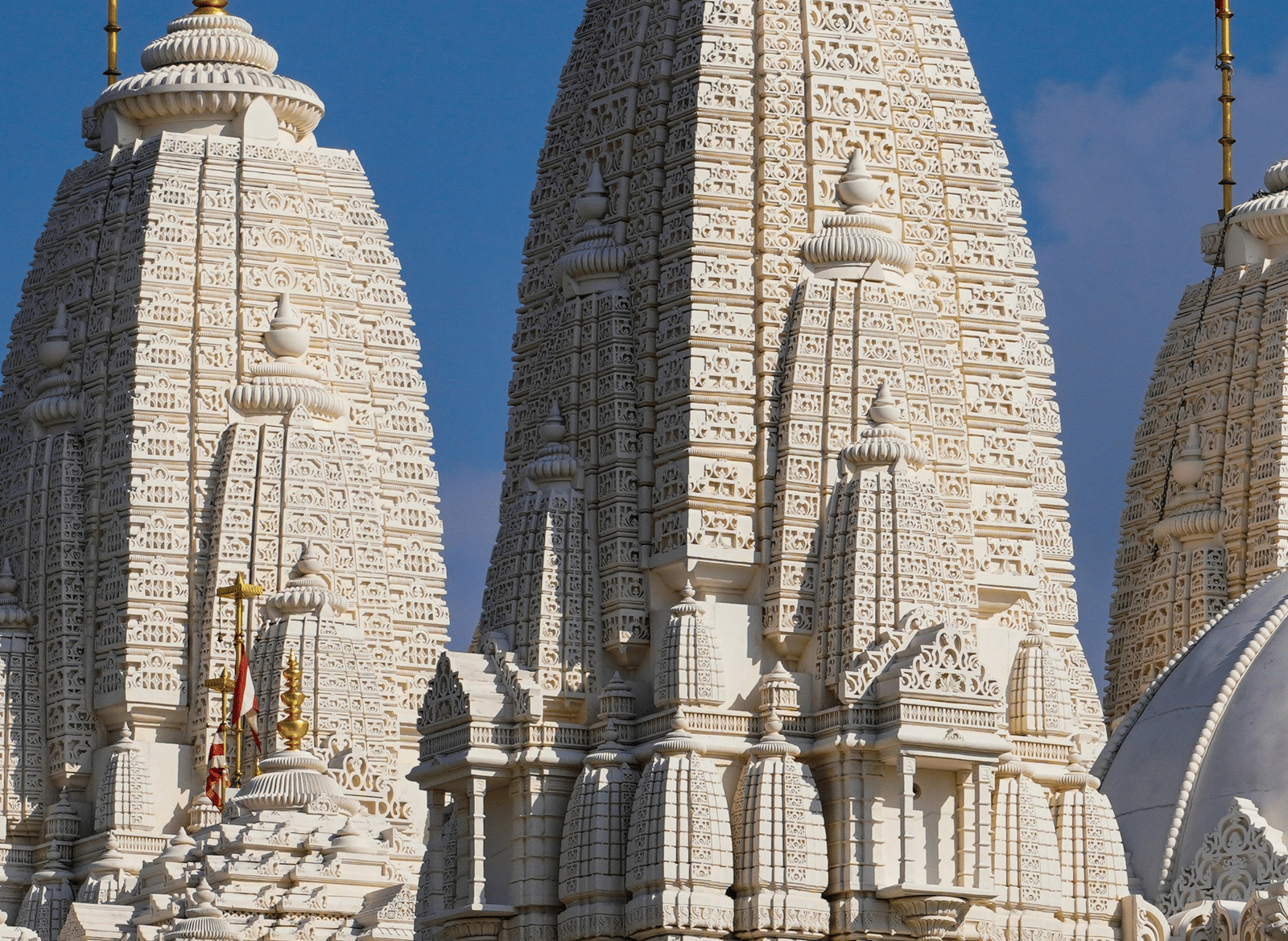A white marble temple spires rise against a clear blue sky, showcasing intricate carvings and traditional architecture.