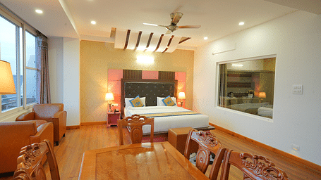 A side angle shot of the hotel suite with a king-sized bed, a seating area with a sofa, a dining table, and a flat-screen TV | DLS Hotel Shiva Sanctuary & Spa, Dharamshala