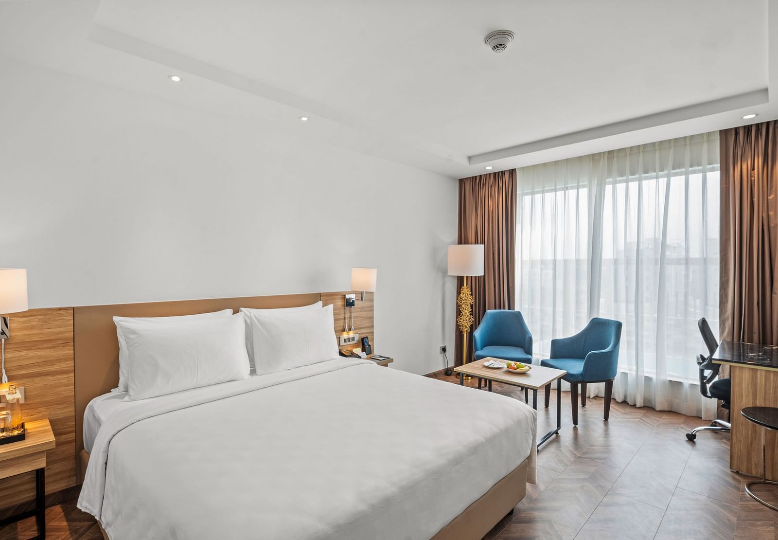 An image of a king size bed and chairs next to a huge window at Grand Vijayawada by GRT Hotels.