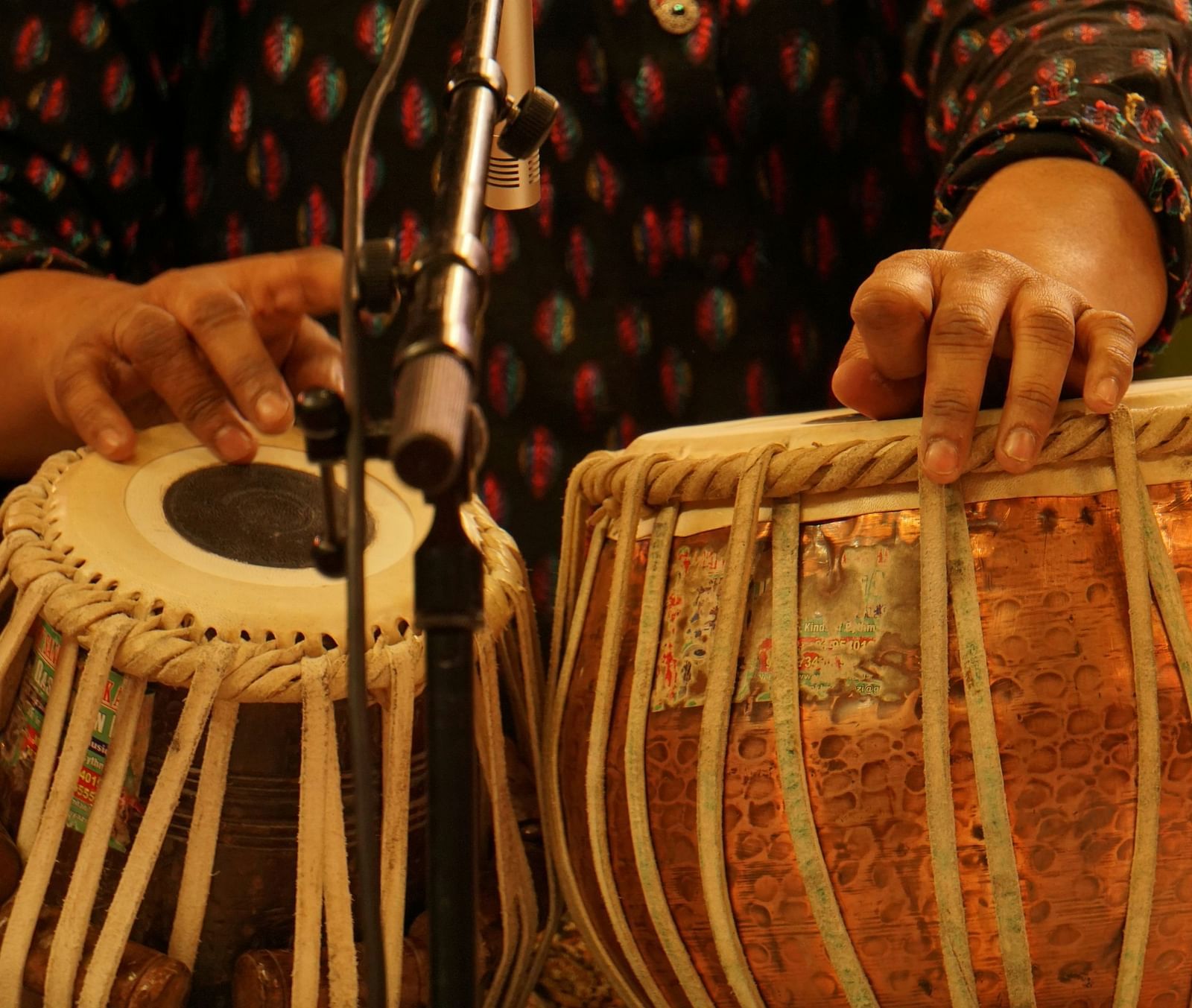 Close up shot of a person playing tabla with a mic placed in front of it.