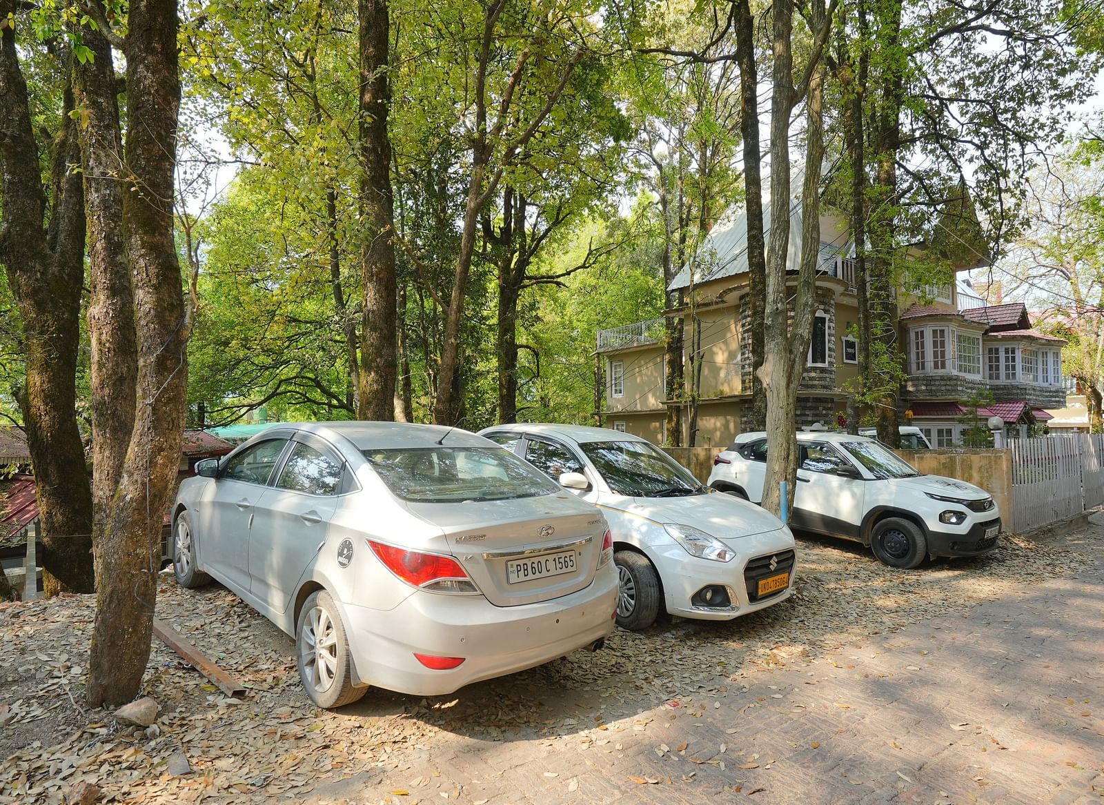The parking area at DLS The Emerald, Nainital where three cars are parked surrounded by trees and greenery