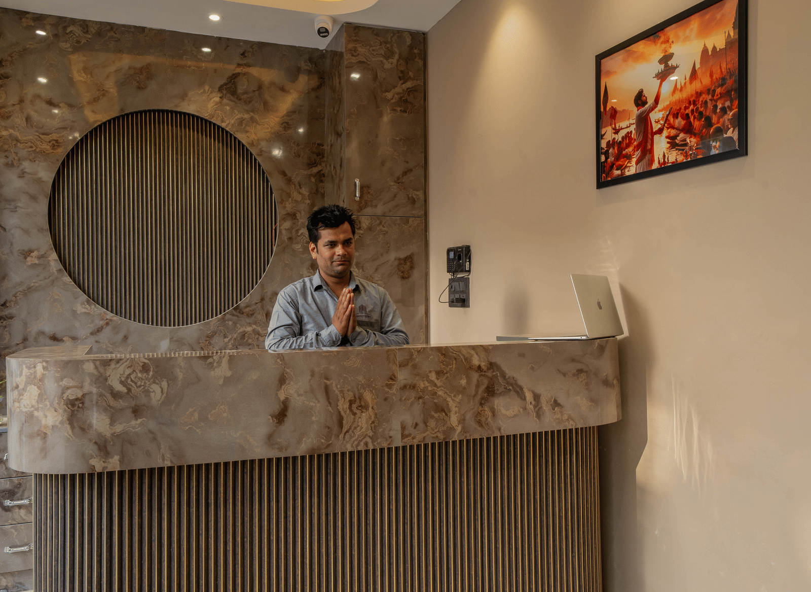 Hotel reception area with a contemporary wooden circular design element on the wall and a staff member standing behind the desk - Perfectstayz Value Aalaya Suites, Haridwar