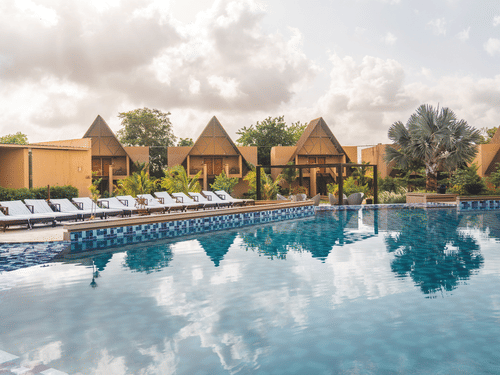 A view of Jagira Ananta Elite, a Gir property, featuring a sparkling swimming pool in the foreground with the resort in the background.
