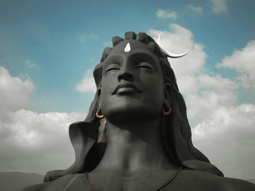 The Adiyogi statue captured from a low angle with dramatic clouds overhead.