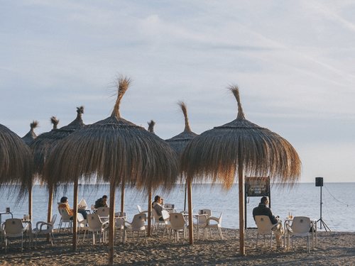 a group of people listening to a man singing and playing guitar on a beach