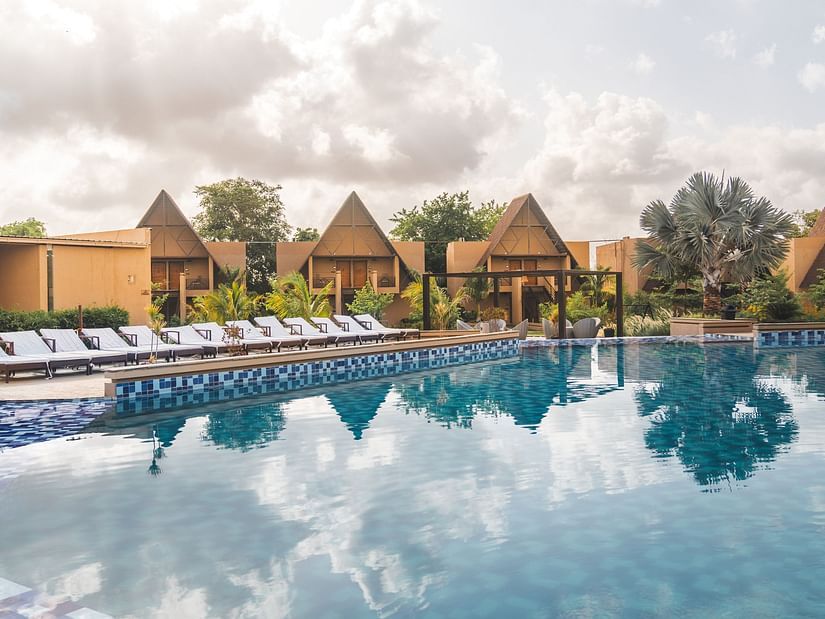 A view of Jagira Ananta Elite, a Gir property, featuring a sparkling swimming pool in the foreground with the resort in the background.