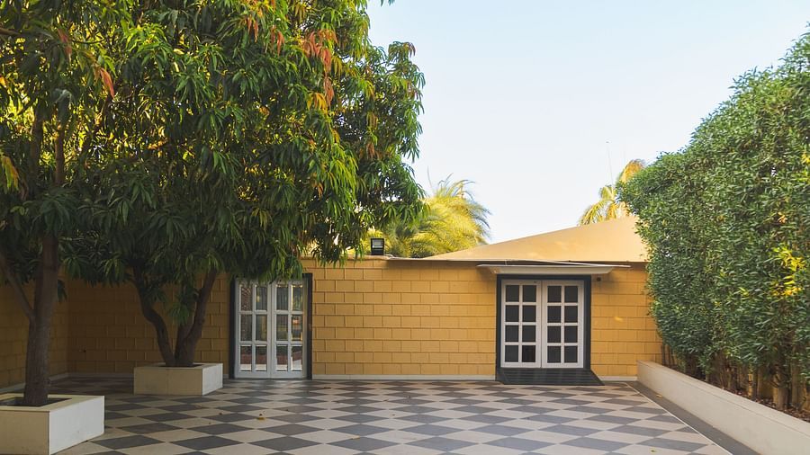 A part of exterior area at The Garden Ananta Elite, showing checker board floors, ambitious trees, and window panes painted with white borders that are attached to the yellow building behind.