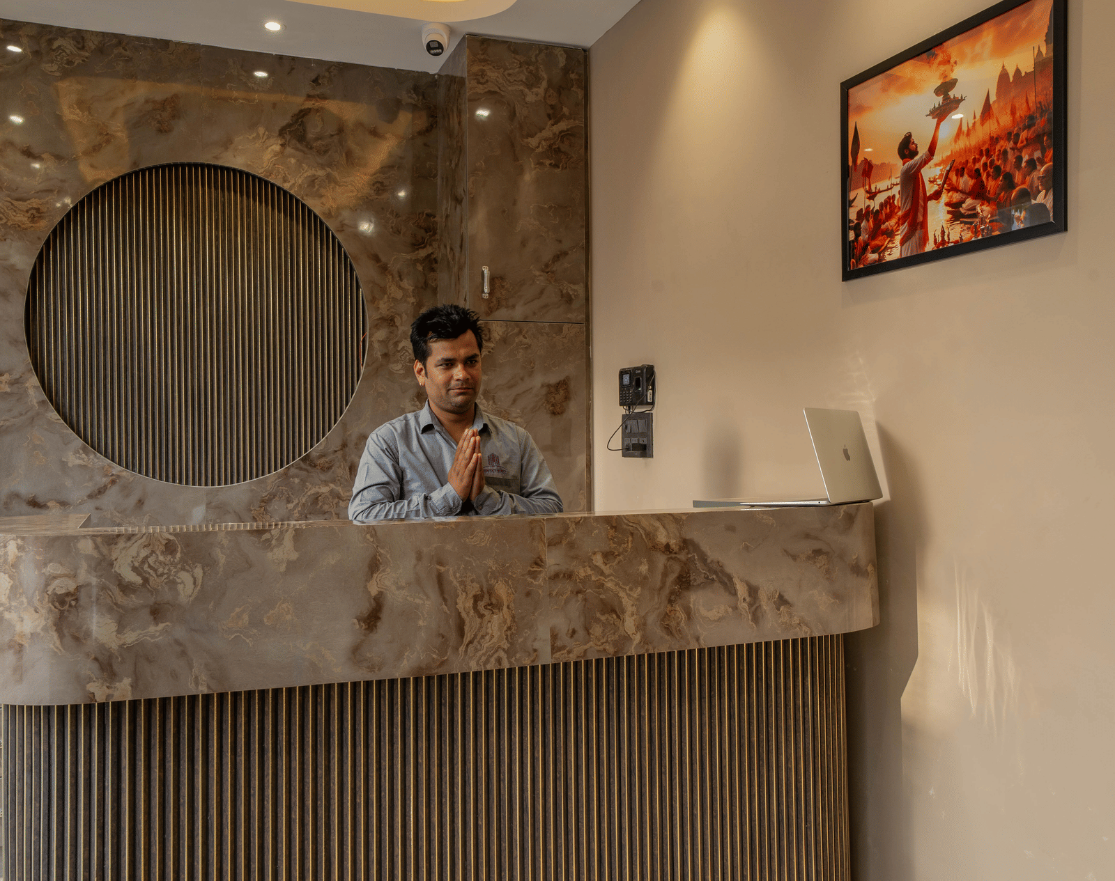 Hotel reception area with a contemporary wooden circular design element on the wall and a staff member standing behind the desk - Perfectstayz Value Aalaya Suites, Haridwar