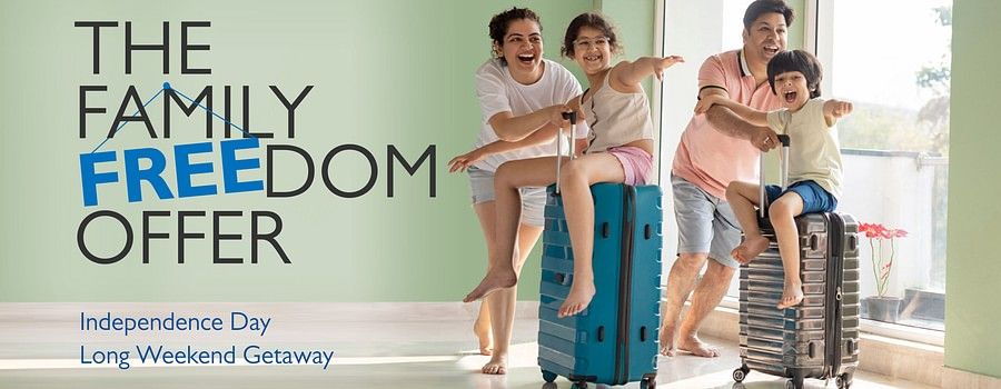  A joyous family with two children poses on suitcases, advertising Family Freedom Offer at Sarovar Hotels for an Independence Day long weekend