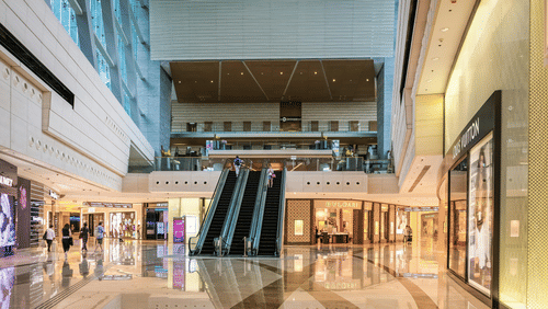 The interior of a modern, multi-level shopping mall with escalators, polished floors, and storefronts on either side.