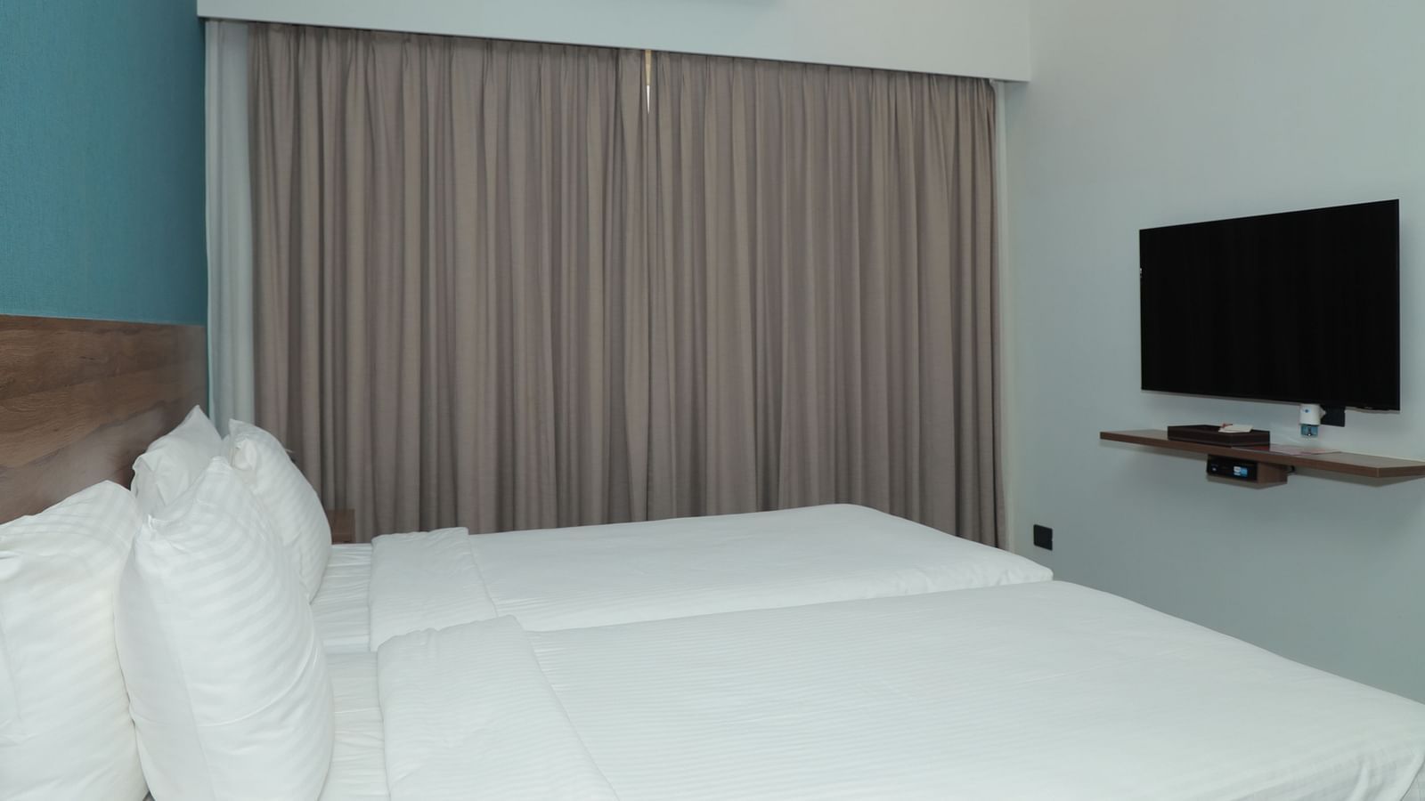 An image of a large bed positioned in front of a wall-mounted television in our Deluxe Rooms in Tuticorin - Regency Tuticorin by GRT Hotels