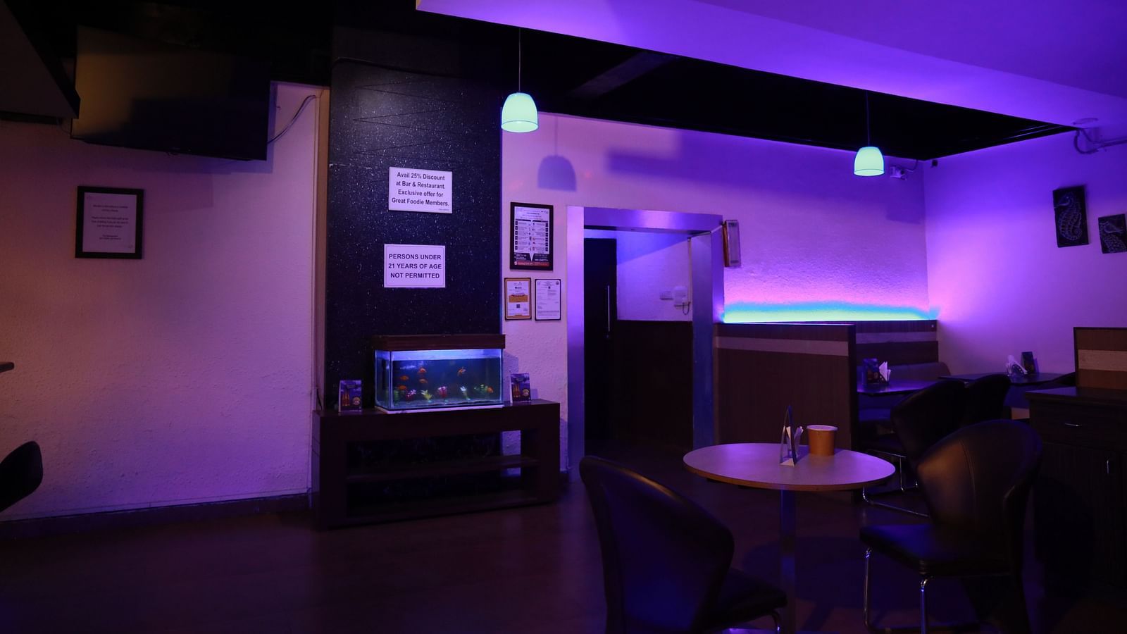An image of a corner space in our moodily lit bar, featuring discounts displayed on the wall above a fish tank - Regency Tuticorin by GRT Hotels