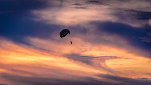 a person parasailing with different hues in the sky after a sunset