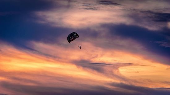 A person parasailing with different hues in the sky behind him