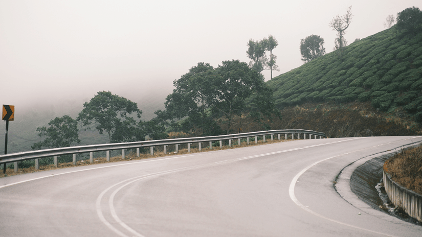 An empty highway curve with mountains in sight under a misty sky