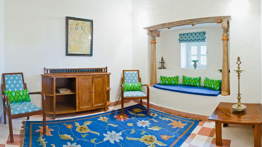 A room with two chairs, a cabinet, a window with cushioned seating, a rug, and a table at Tijara Fort-Palace - 19th Century, Alwar.