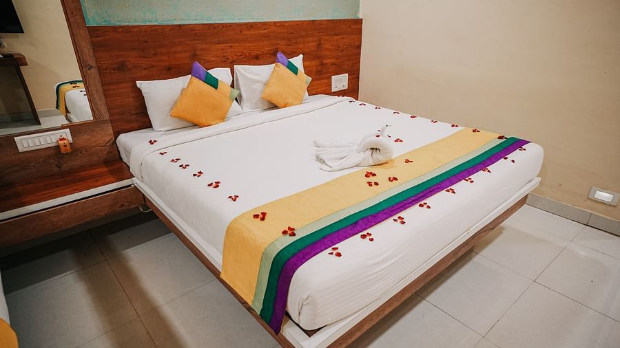 An image of a deluxe room featuring a bed, bed side table, and a mirror - Nisarga Lake Resort