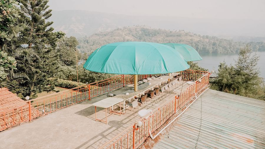 An image of a rooftop bar at Nisarga Lake Resort featuring chairs, tables and umbrellas, offering views of the mountains and lake