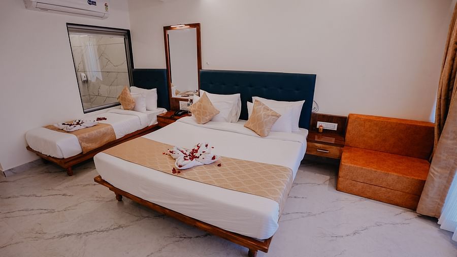 An image of a premium room featuring a queen bed and a single bed along with bed side tables, a couch, and a mirror - Nisarga Lake Resort