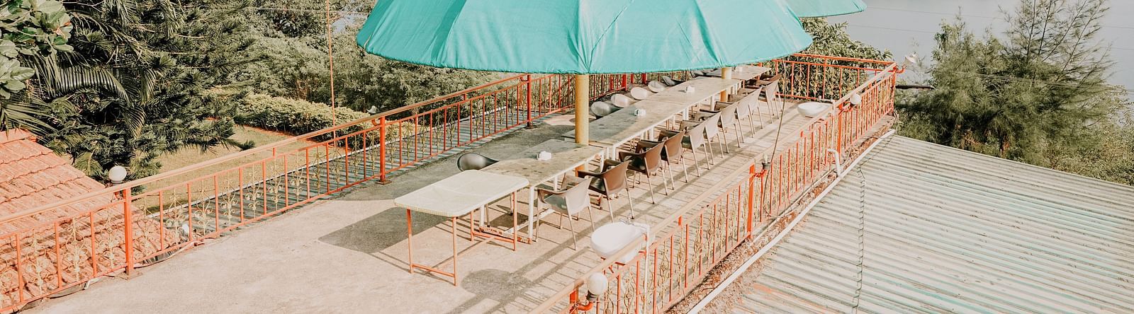 An image of a rooftop bar at Nisarga Lake Resort featuring chairs, tables and umbrellas, offering views of the mountains and lake