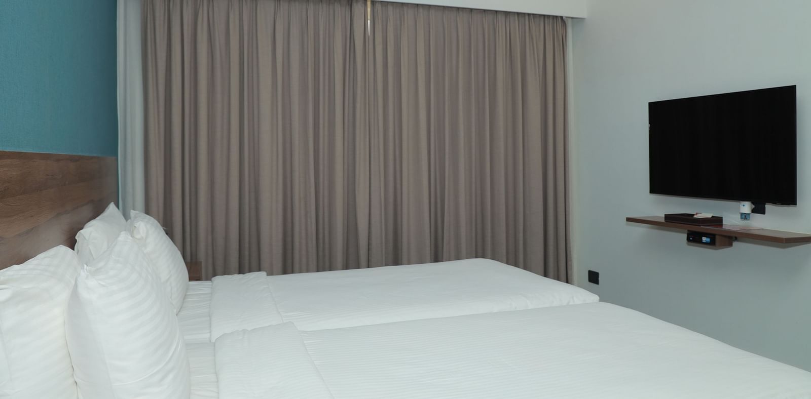 An image of a large bed positioned in front of a wall-mounted television in our Deluxe Rooms in Tuticorin - Regency Tuticorin by GRT Hotels
