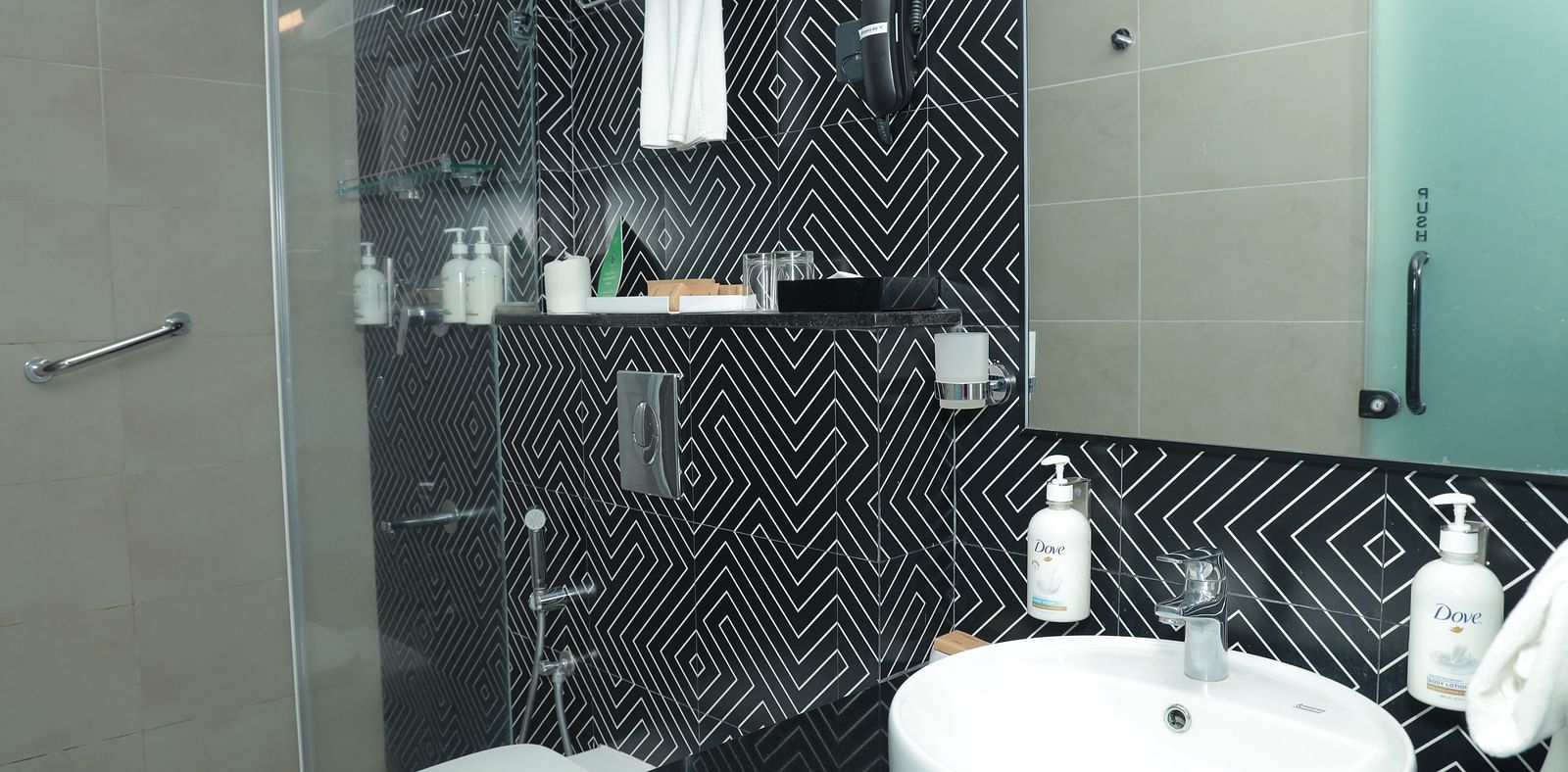 An image of a vanity counter with toiletries, a sink and, a mirror placed beside a shower cubicle separated by a glass door - Regency Tuticorin by GRT Hotels