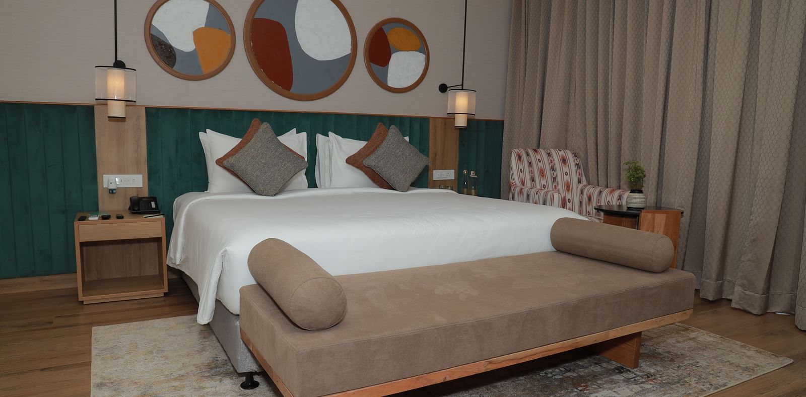 A bed with a bench and a beautiful wall painting above the headboard in our suite at Regency Tuticorin - Thoothukudi Hotel Rooms