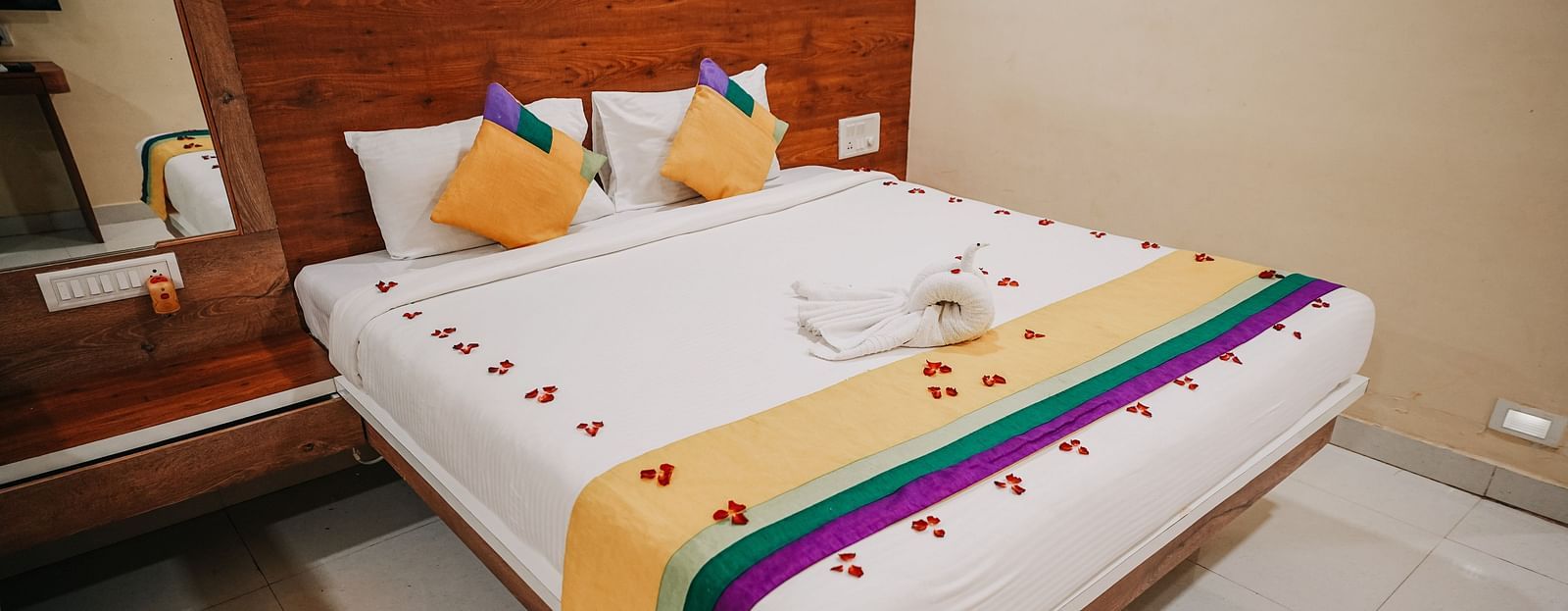 An image of a deluxe room featuring a bed, bed side table, and a mirror - Nisarga Lake Resort
