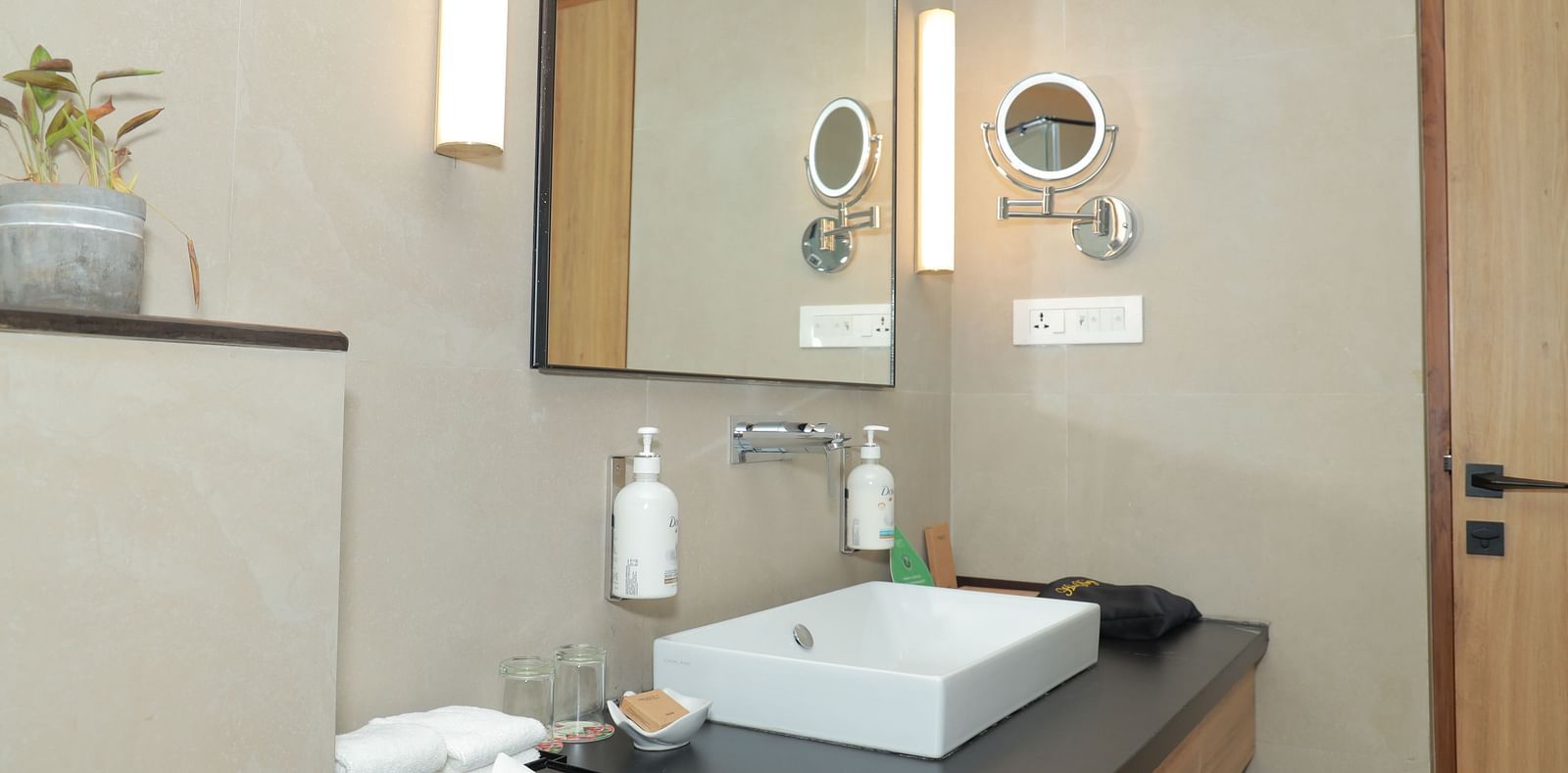 An image of the vanity counter in our washroom, with toiletries placed near the sink and a self-magnifying mirror on the wall - Regency Tuticorin by GRT Hotels