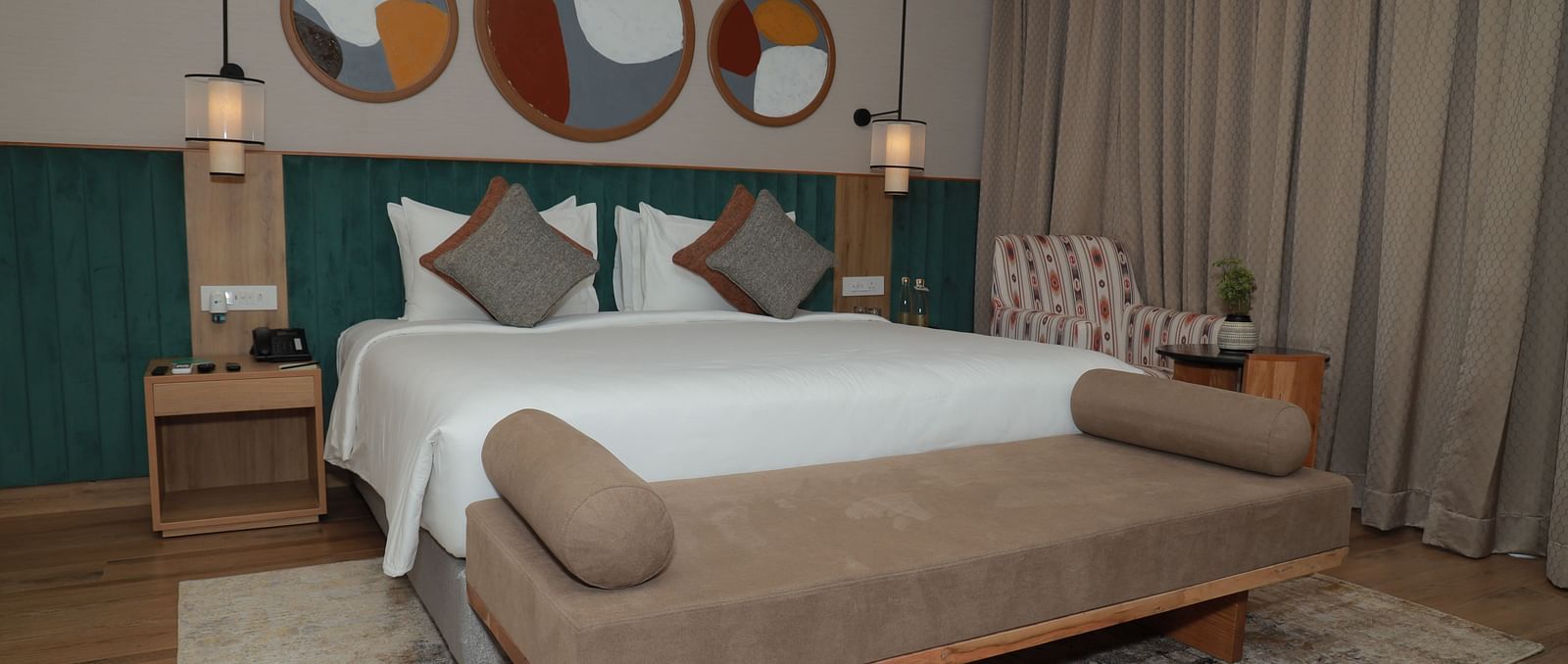 A bed with a bench and a beautiful wall painting above the headboard in our suite at Regency Tuticorin - Thoothukudi Hotel Rooms